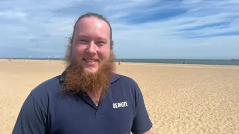 Andrew Turner/BBC Elric Turbett standing next to the beach at Great Yarmouth