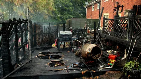 The charred remains of a veranda ravaged by fire. Several items have been damaged by fire, including a cement mixer and a barbeque.