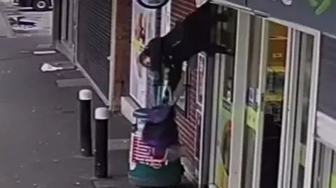 CCTV shows a woman hoisted into the air due to her coat becoming stuck in shop shutters