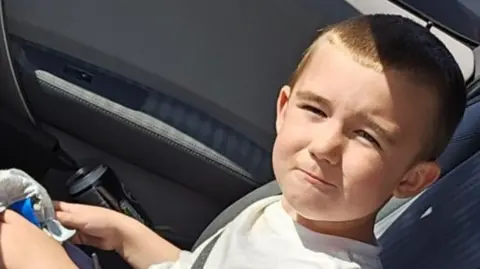 Family handout Lincoln Button is sitting in a car. He is squinting into the sun as he poses for the camera. He has cropped brown hair and is wearing a white T-shirt.