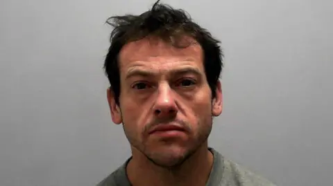 A police mugshot of Dale Blaney, a man with short dark brown hair and stubble, wearing a grey jumper, against a neutral backdrop.