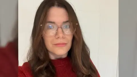 A selfie taken by Zenobia, wearing glasses with a red jumper.