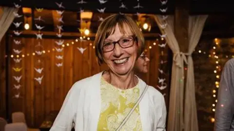 Smiling woman in glasses wearing a patterned top and white cardigan