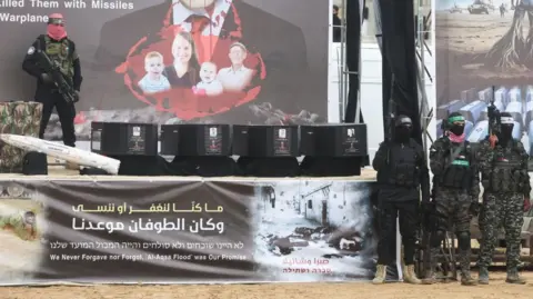 Reuters Four coffins on a stage flanked by armed Hamas fighters in Khan Younis, southern Gaza (20/02/25)