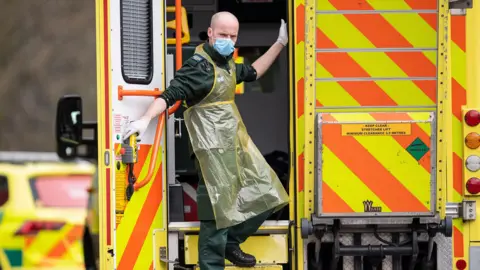 Getty Images Paramedic in mask and PPE on back of ambulance