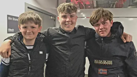 Three boys standing side-by-side with their arms around eachother.