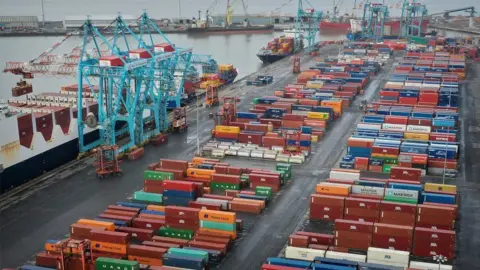 An aerial view of Seaforth docks. Rows of different coloured shipping containers sit next to a series of blue cranes used to load and unload containers.