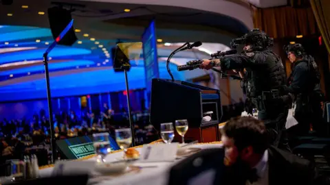 An officer points a large gun with wine visible in the foreground
