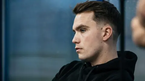 Joe Ricciardi A side on view of Niall Quiggin, who has short dark hair and is wearing a black hoodie. 