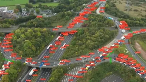 Road with a circular road on the top. There are many vehicles on several roads and they are all highlighted with dark orange strips which gives information on them. 