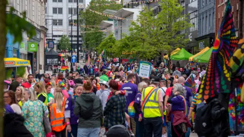 City of Wolverhampton Council A crowded city centre street with brightly coloured bunting. Some people are carrying Pride flags, some are carrying banners, most are wearing bright coloured clothes