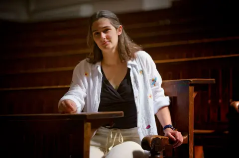 BBC Amanda Cole sits on one of the lecture theatre benches at Cambridge University