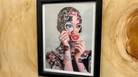 BBC A picture of a woman in a frame. She is covered in stickers.