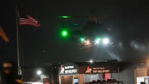 AFP via Getty Images A helicopter flying in darkness with the US flag on a pole to the left and two "VIP Heliport" signs