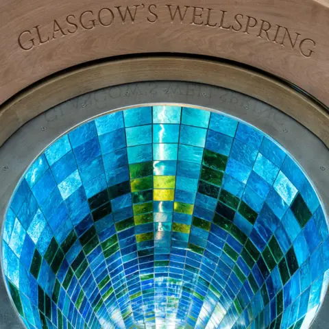 Alasdair Smith A view from above into the well shaft shows the myriad of stunning blues and greens of the tiles. Carved in the surrounding wodd are the words "Glasgow's Wellspring".