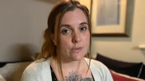 Sitting in the living room where her mum was murdered, Lucie Lambourne, in a beige cardigan and her hair tied back, looks at the camera lens.
