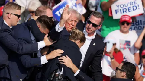 Reuters Secret service bodyguards crowd around a waving Donald Trump and try to usher him off stage after he was shot at during a rally in Butler, Pennsylvania on July 13