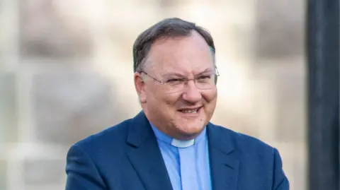 Getty Images Rev Dr Trevor Gribben, a man with short dark grey hair, wearing a navy suit jacket, a light blue shirt and glasses.