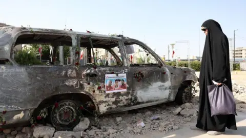 A veiled Iranian woman stands next to an ambulance of the Iranian Red Crescent Society (IRCS) that was destroyed in an Israeli strike, in Tehran, Iran, 23 June 2025.