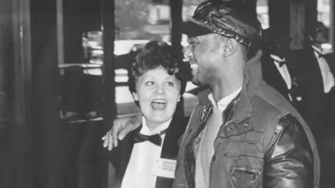 Getty Images Washington DC, December 15, 1985. A refugee is escorted to his "fake" Redskins tickets from a US Marshal in a tuxedo.