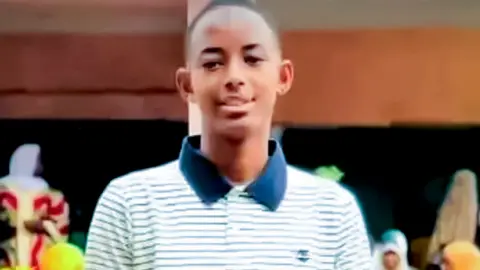 Mamadou Djouma Bah smiling, wearing a striped white and blue T-shirt