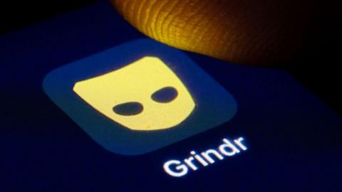 A thumb hovering above the grindr app logo