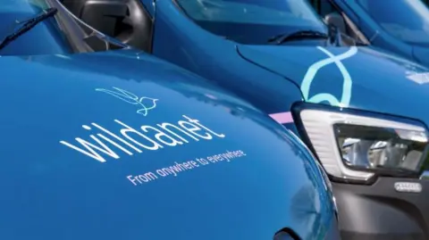 A fleet of Wildanet vans parked up. All the vans have the company's logo on their bonnets. The vans are navy blue.