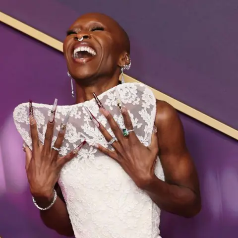 Getty Images Cynthia Erivo wore her trademark long, bejewelled fingernails with a white, lace dress