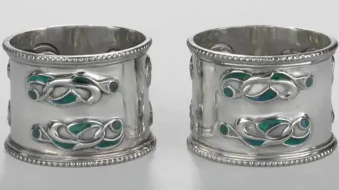 Two small, round silver pieces featuring Celtic-inspired designs in green and blue.