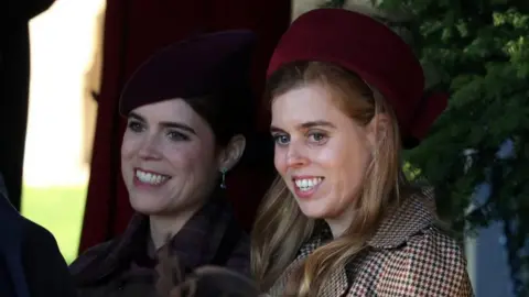 Reuters Princesses Beatrice and Eugenie at the Royal Family's Sandringham Christmas service. Eugenie wears all black while Beatrice wears a chequered coat and red hat. 