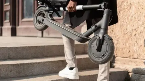 A person carries an e-scooter up some steps in an unknown city.