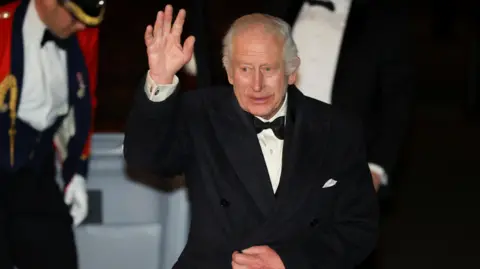 Reuters King Charles lifts a hand to wave as he walks from his car into the Royal Albert Hall