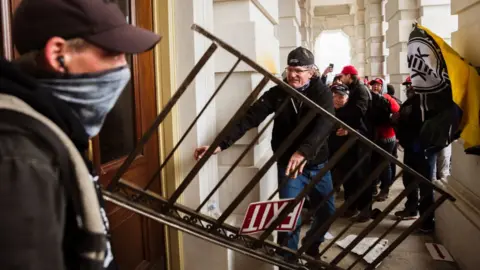 AFP A member of a pro-Trump mob bashes an entrance of the Capitol Building in an attempt to gain access on January 6, 2021 in Washington, DC.