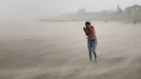 Getty Images A woman seeks cover from wind, blowing sand and rain whipped up by Hurricane Dorian as she walks on the beach on September 2, 2019 in Cocoa Beach, Florida.