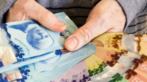 Getty Images A man holding up Canadian dollar bills