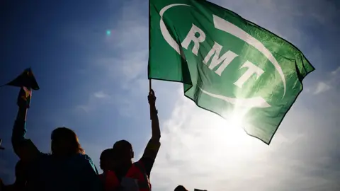 Ben Birchall / PA Media A green RMT flag is held in the air on a picket line outside Bristol Temple Meads station, as members of the Rail, Maritime and Transport union begin their nationwide strike in a bitter dispute over pay, jobs and conditions.