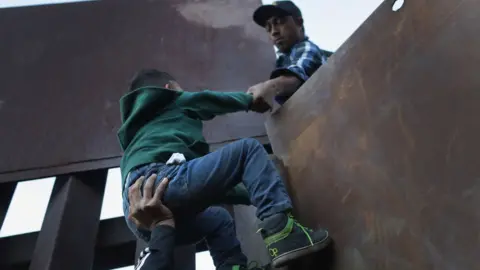 Getty Images A boy is hoisted by fellow members of the migrant caravan over the US-Mexico border fence
