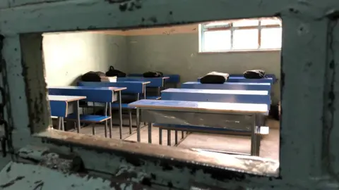 BBC Some blue desks with books on in a classroom