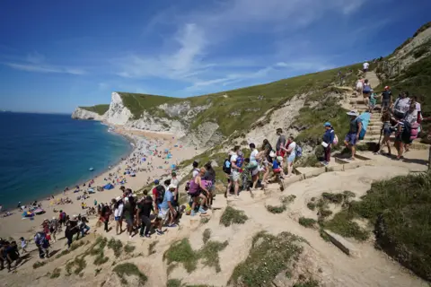 Andrew Matthews / PA Media People make their way down steps to Durdle Door beach in Dorset