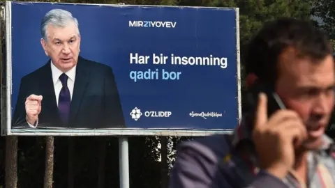 Getty Images A man talks on a mobile phone in front of a campaign billboard of Uzbekistan's President and presidential candidate Shavkat Mirziyoyev