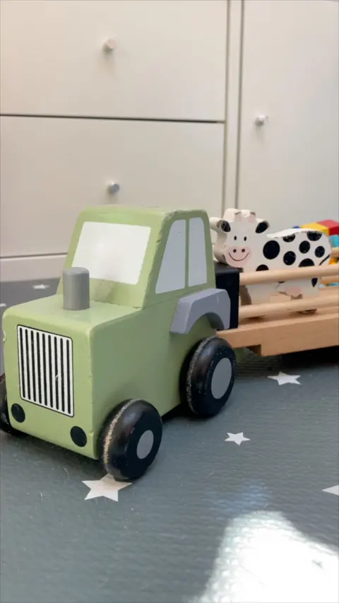 A green toy tractor pulling a toy trailer carrying a toy cow