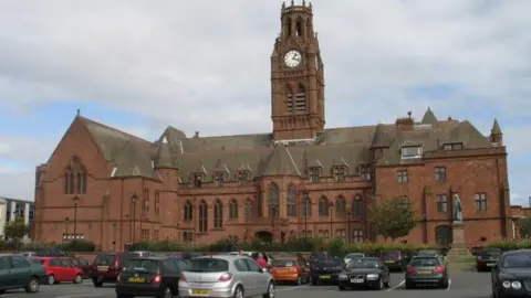 GEOGRAPH / Gerald Massey Barrow Town Hall. The building is made from red sandstone and features a large clock and gothic windows. There are several cars parked in front. 