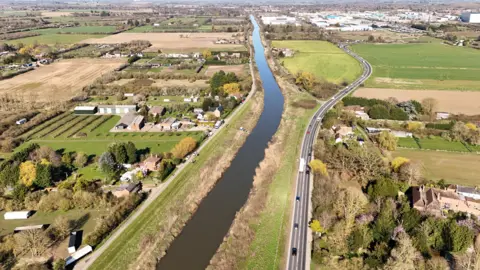Qays Najm/BBC An aerial image of the A47 running next to the river, with North Brink on the other. The area is mainly rural with a few houses and industrial buildings in clusters.