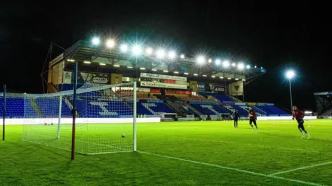 It is night-time and the lights are on at Inverness Caledonian Thistle's stadium. The lights illuminate the main stand  