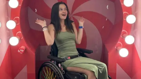 Maddie Haining Maddie Haining is wearing a olive green dress while sitting in her wheelchair. 