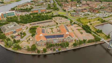 View looking over Teesdale Business Park taken by a drone. There are many industrial buildings located next to a stretch of water.