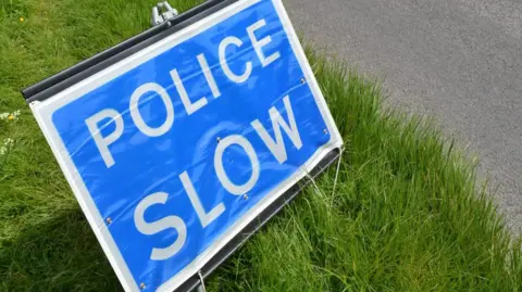 Getty Images A blue "police slow" sign a grass verge on the side of the road