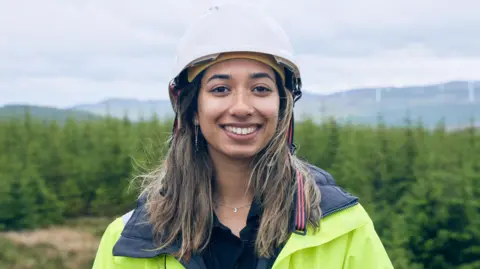 Green Party Eishar Bassan with long brown hair wearing a hard hat and hi-vis jacket