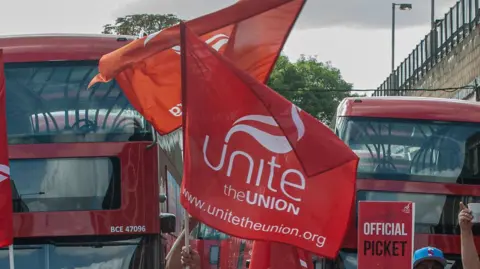 A Unite the Union flag waves outside at a picket line near some buses 