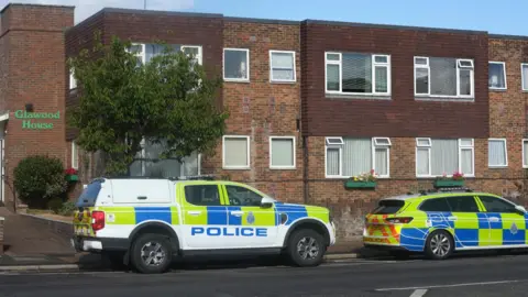 Two police vehicles are parked outside a two-storey residential building